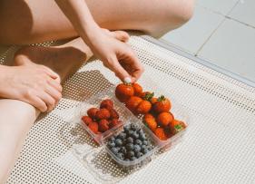 a tray of berries on the edge of a bed and someone reaching for one of the strawberries