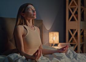 woman meditating on her bed in the dark