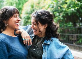 two women laughing, one of them has her elbow on the other's shoulder
