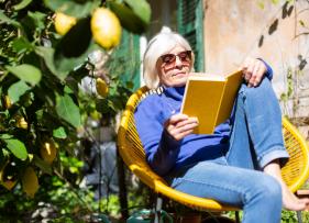 an old lady reading in the sun next to a lemon tree