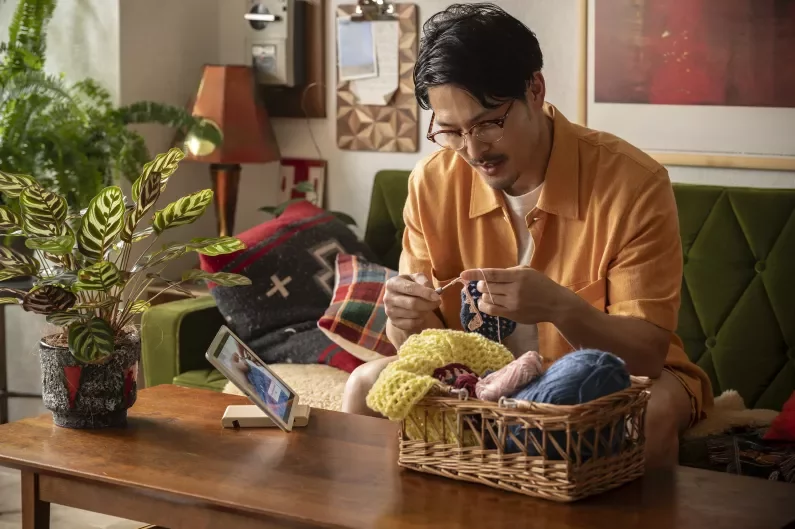 a man knitting at a table with a basket of yarn
