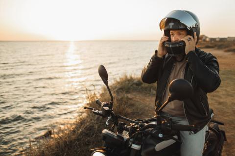 a man taking off a motorcycle helmet on his bike next to water at sunrise