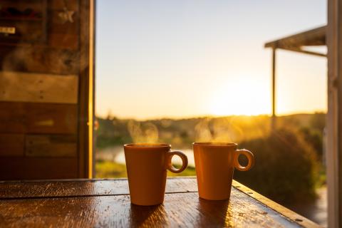 two steaming cups of coffee on a table at sunrise