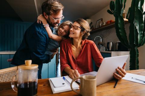 a mom with her laptop, and a dad holding their daughter at a table